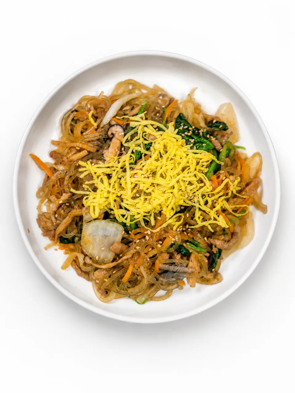 Japchae on a white plate topped with thin egg strips