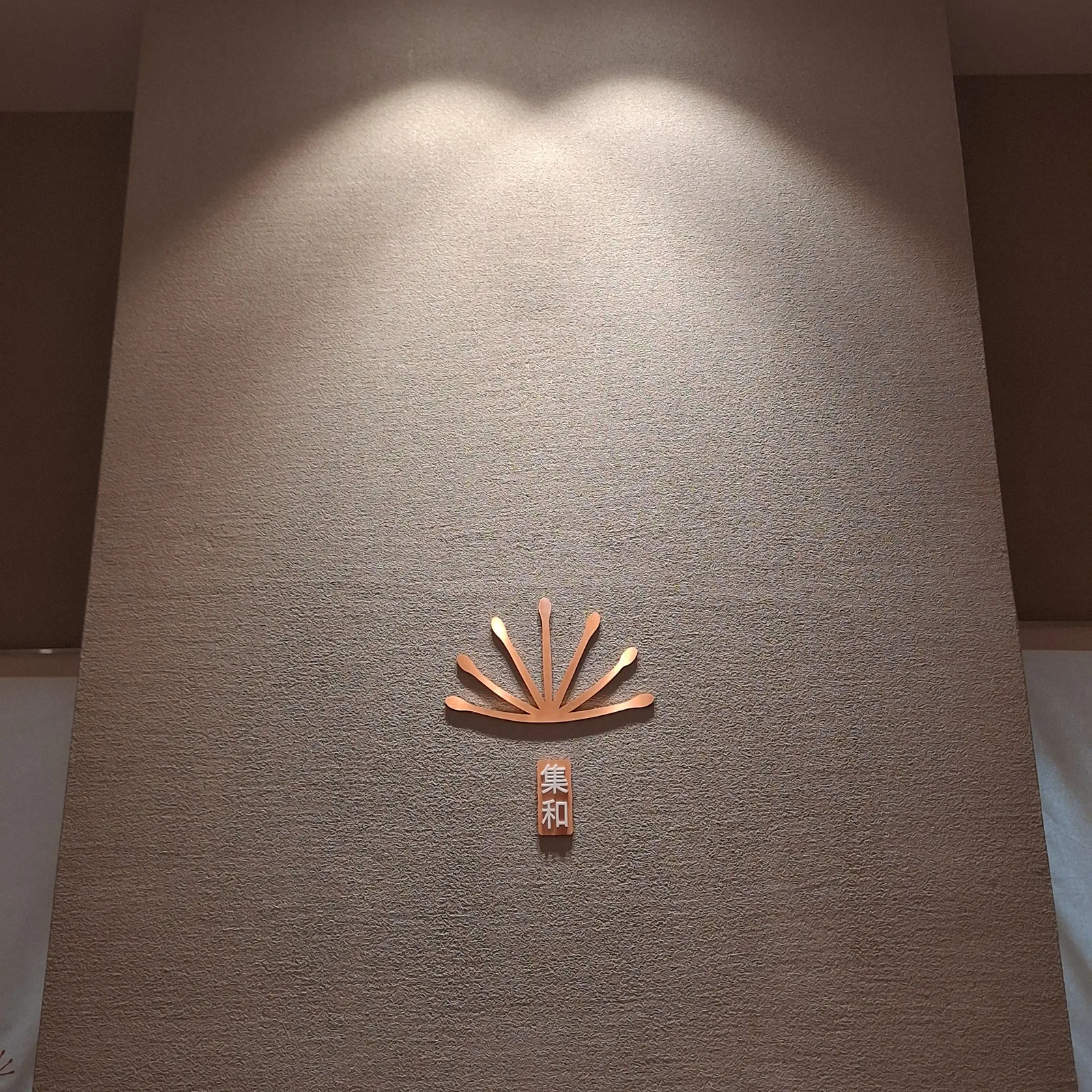 The copper dandelion logo and red seal mounted on a plaster wall
